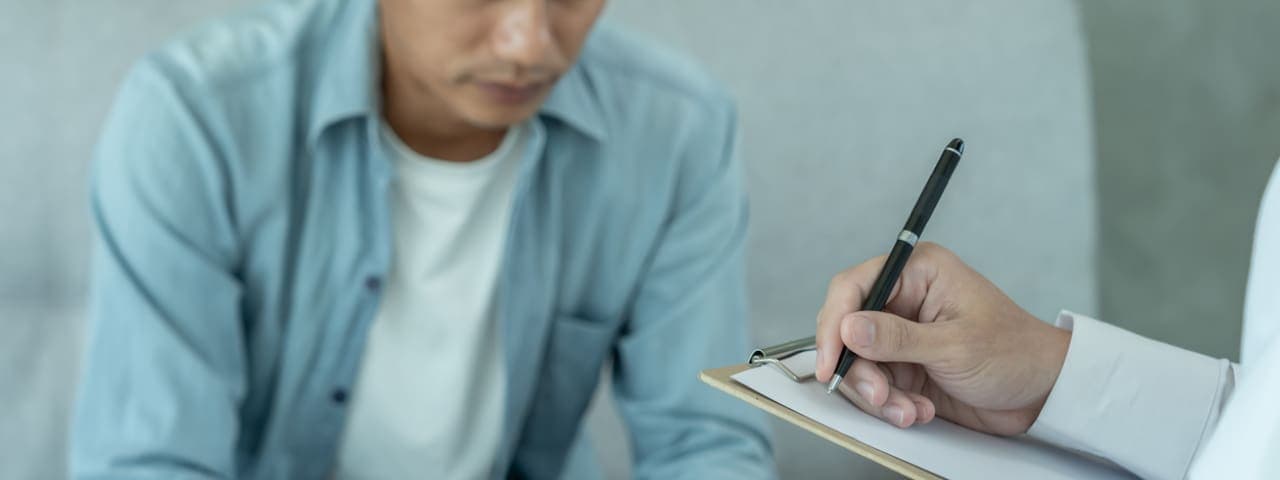 A man is sitting across from psychiatrist recording the patient's condition for treatment.