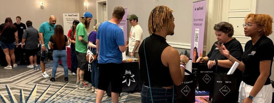In brightly lit conference room with event signage, Leafwell event attendees speak with dispensary staff at tables with giveaway bags
